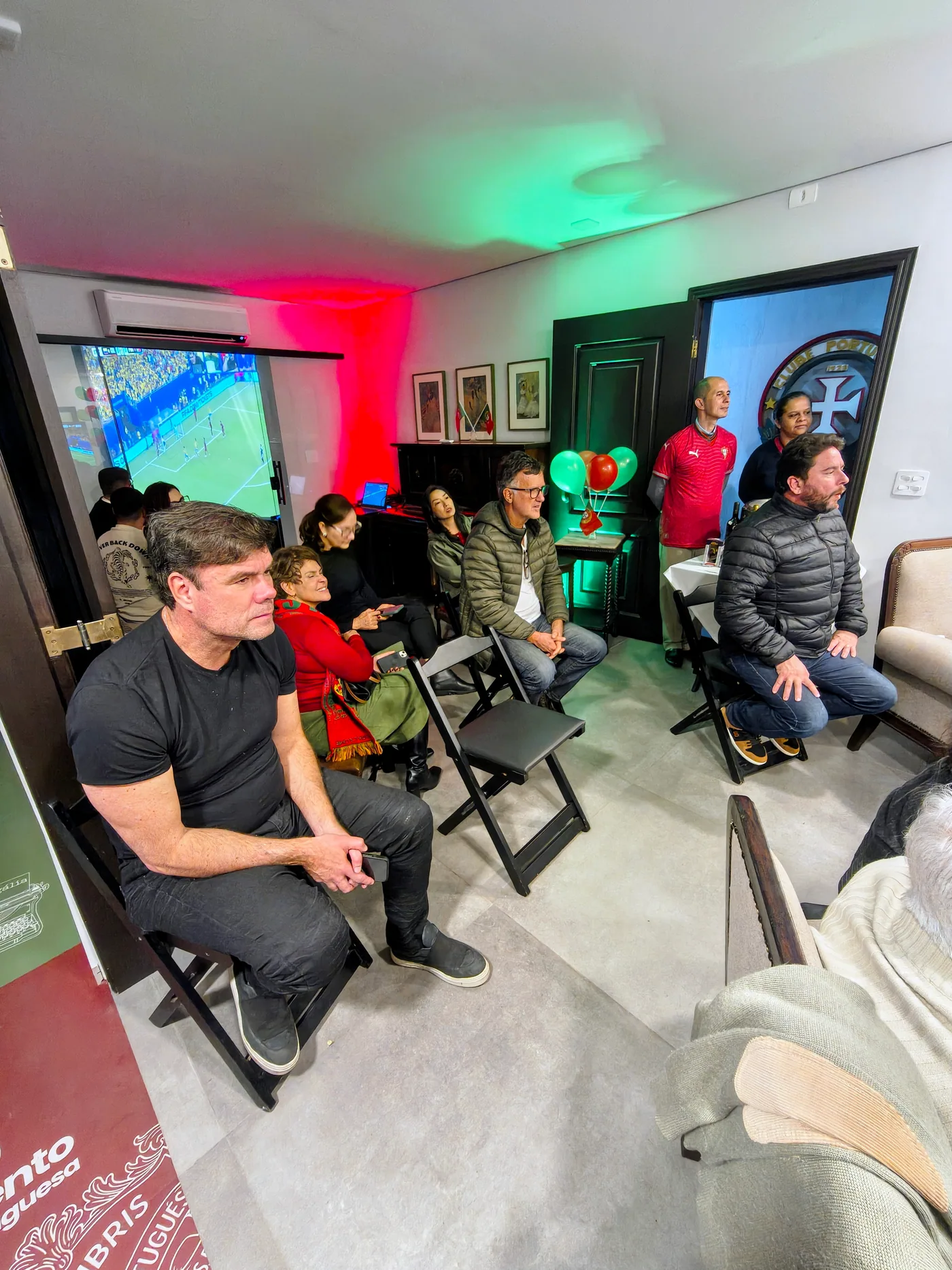 Torcida reunida em sala iluminada com as cores portuguesas